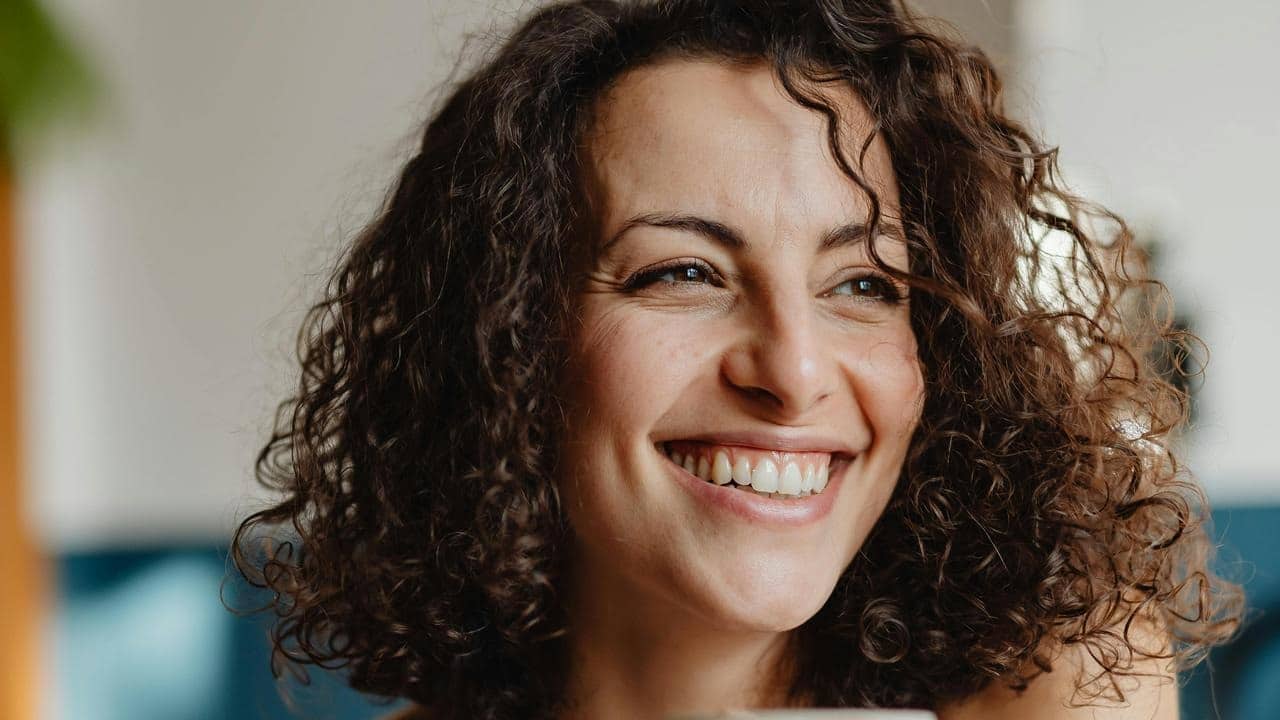 A close-up of a smiling woman with curly hair indoors.