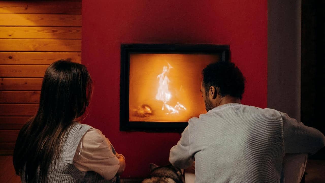 A couple sitting together and watching a fire burning in a fireplace.