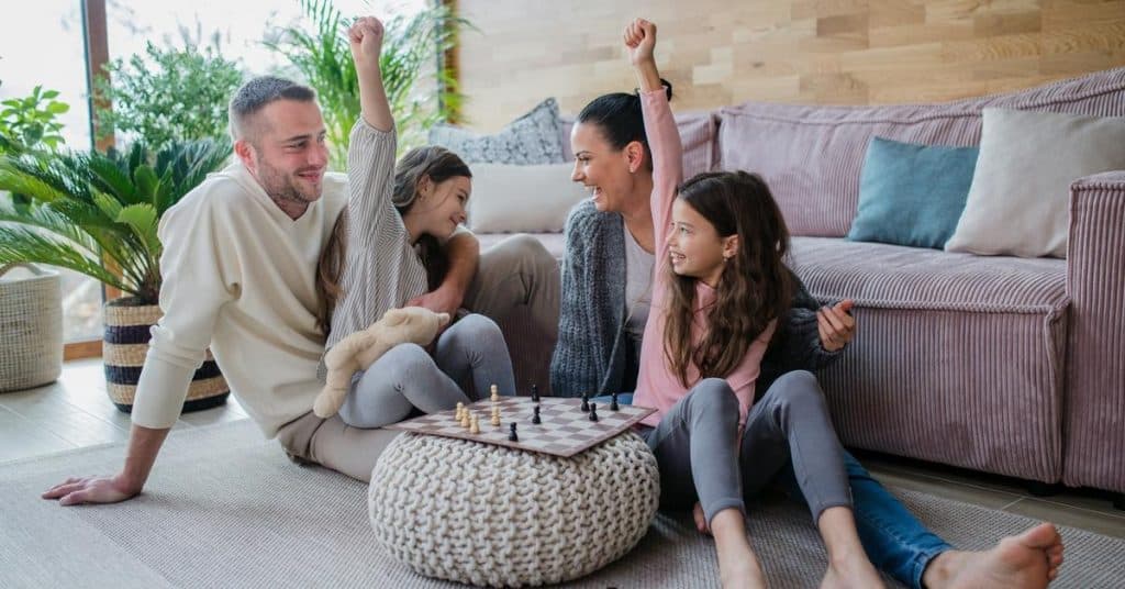 A happy family playing chess on the living room floor, children cheering.