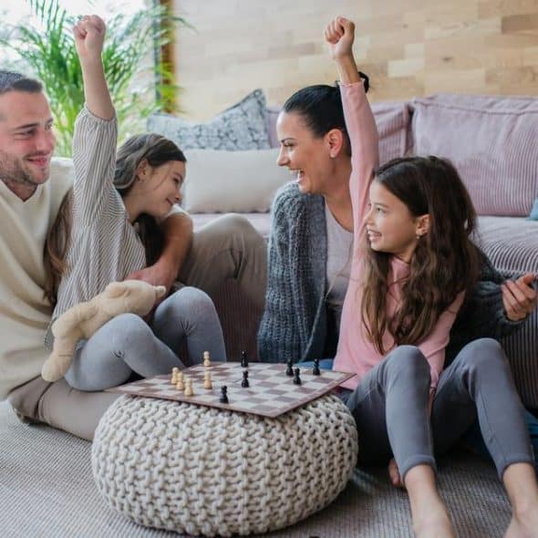 A happy family playing chess on the living room floor, children cheering.