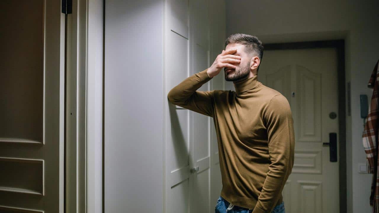 A man standing in a hallway covering his face with his hand.