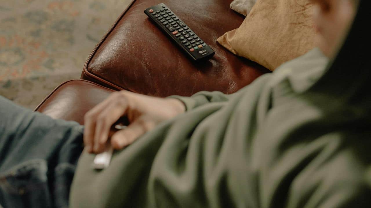 A person lying on a couch with a remote on the cushion nearby.