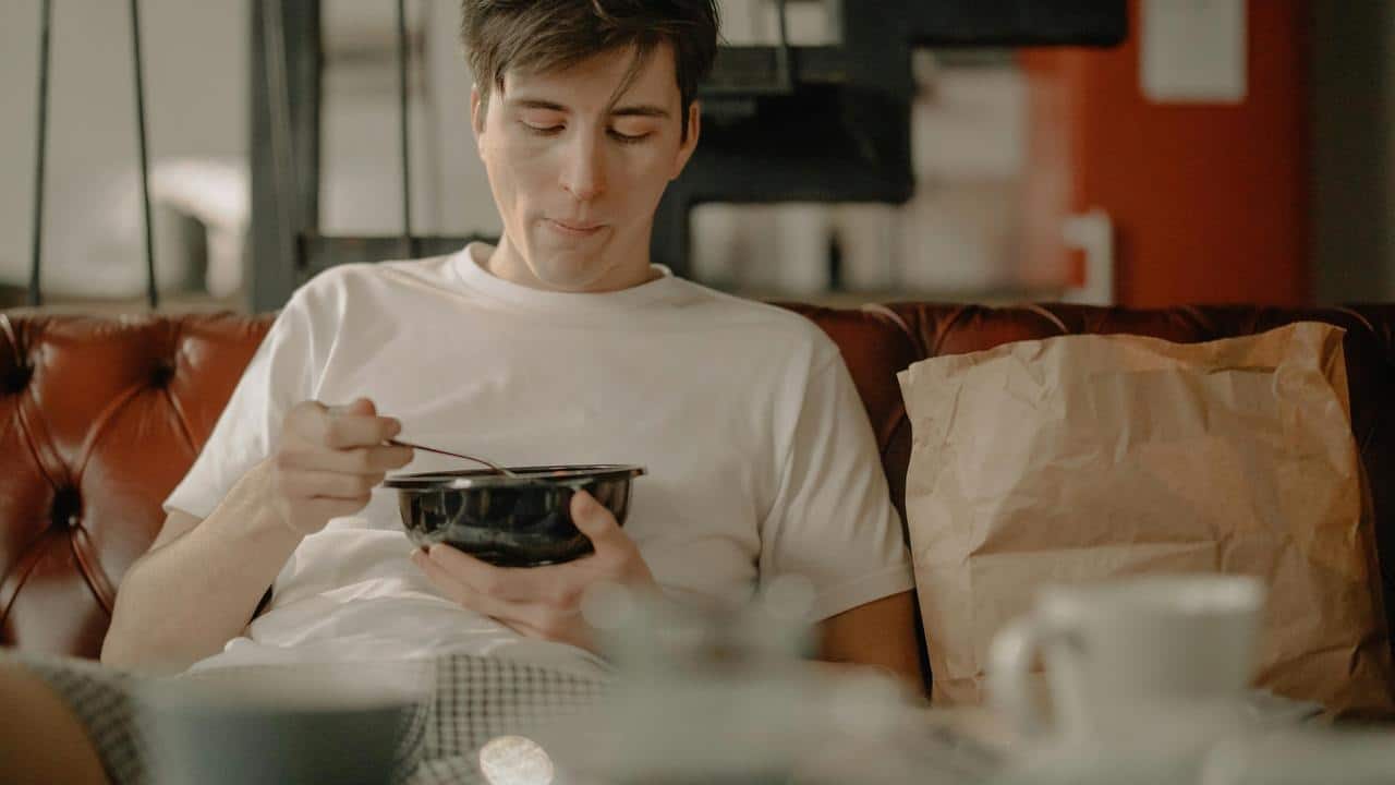 A man sitting on a couch eating from a bowl.