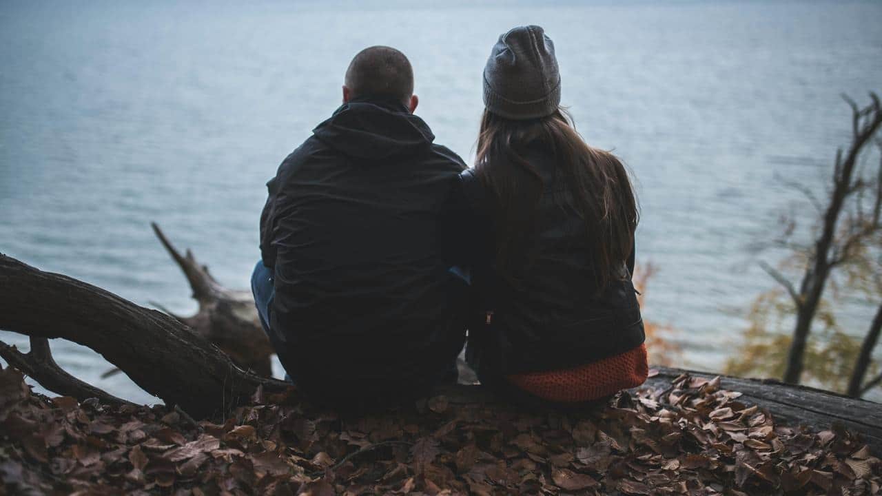A couple sitting on a log by the water.