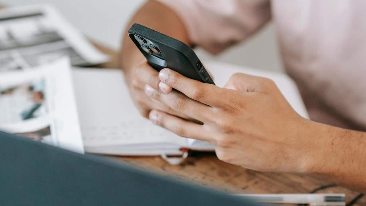 A person holding a smartphone while sitting at a desk with papers.