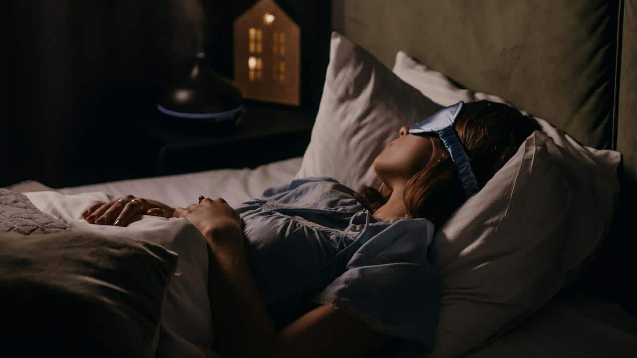 A woman wearing a sleep mask rests in bed at night.