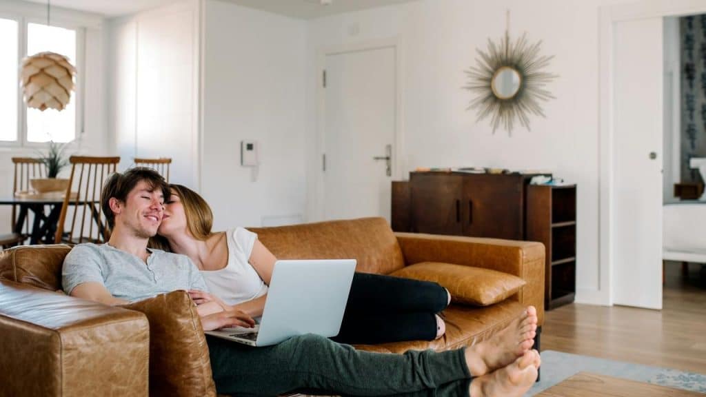 A couple relaxing on a couch while using a laptop at home.