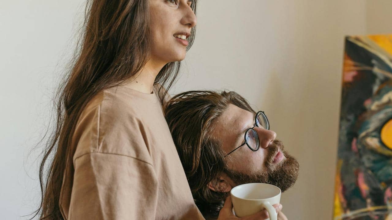 A couple relaxing together, one holding a cup and leaning affectionately on the other.