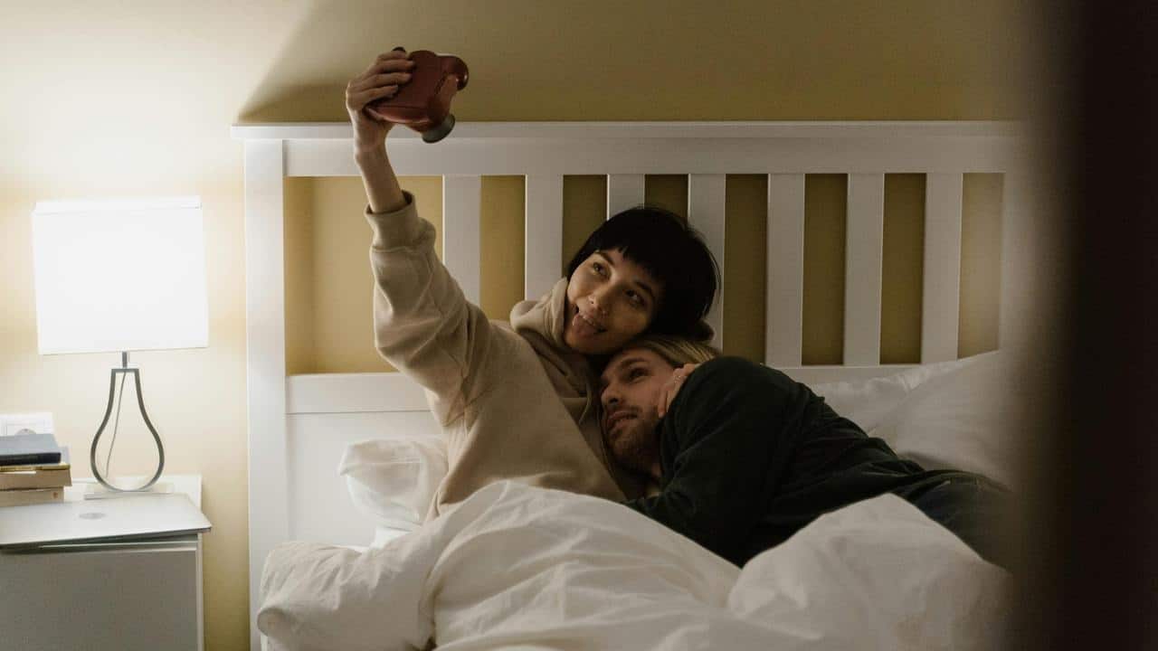 A couple lying in bed, taking a playful selfie together.