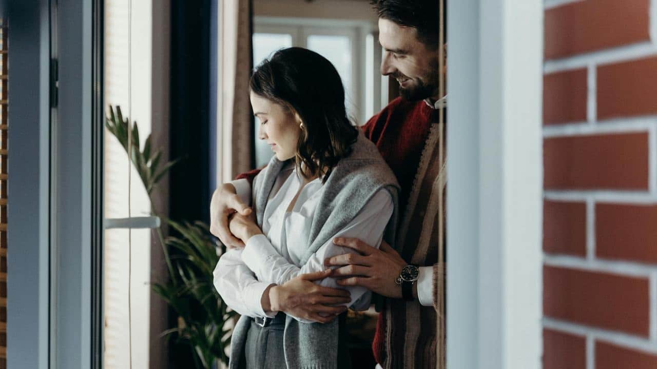 A couple standing by a window, embracing affectionately indoors.