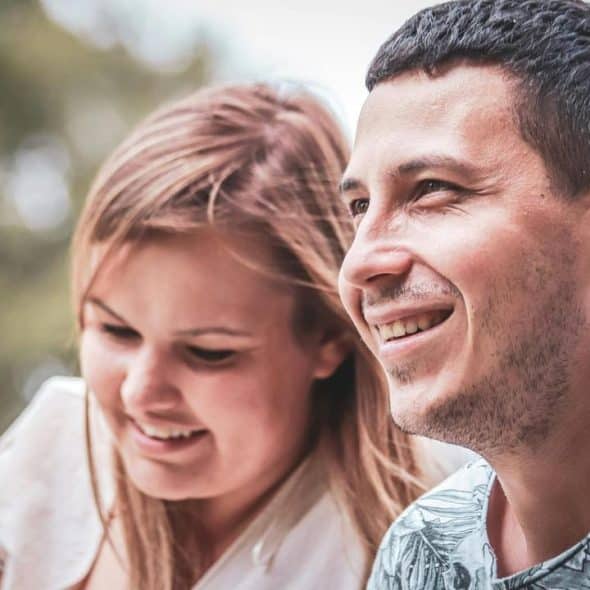 A smiling couple sits outdoors, looking relaxed and happy.