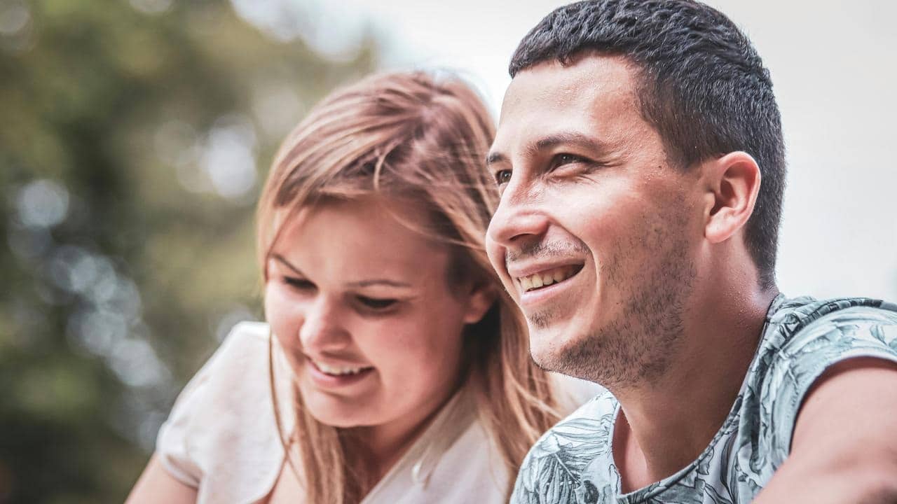 A smiling couple sits outdoors, looking relaxed and happy.