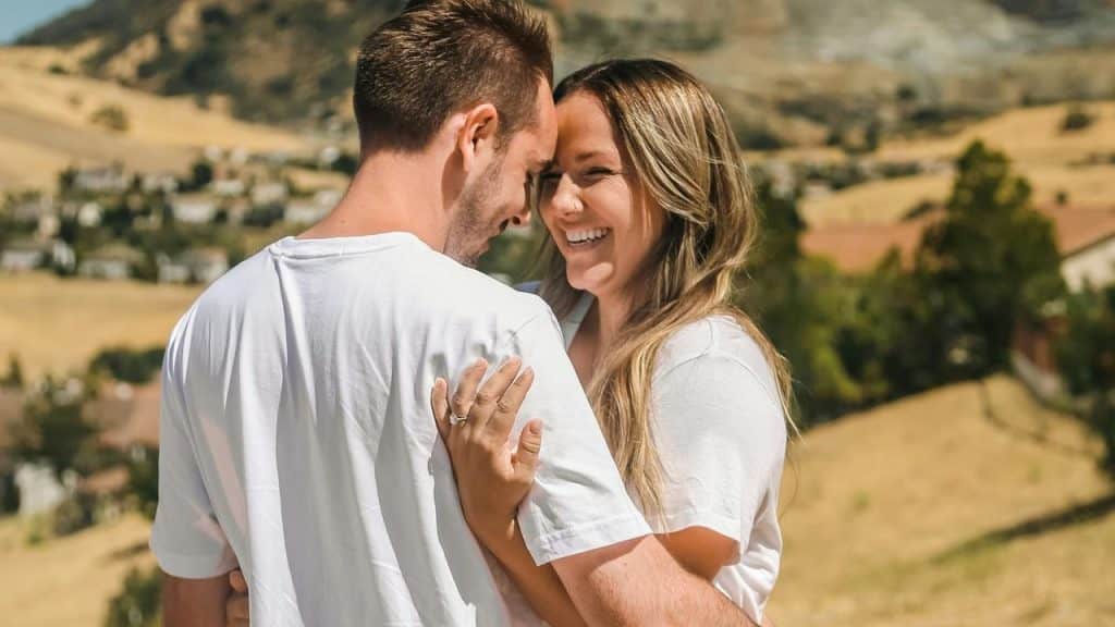 A couple smiling and embracing outdoors in a scenic countryside.
