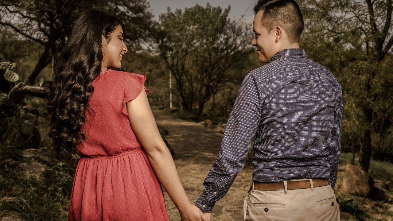 A couple walking hand in hand down a wooded path.