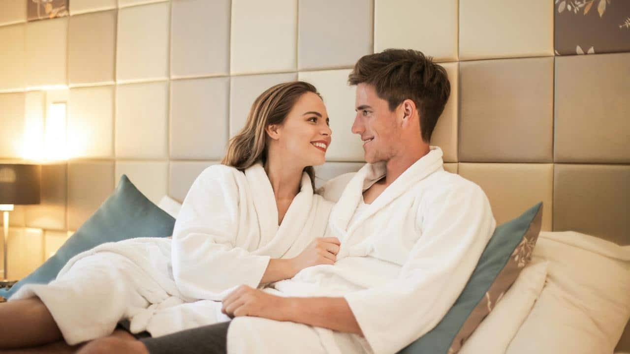 A couple in white robes relaxing together on a bed.