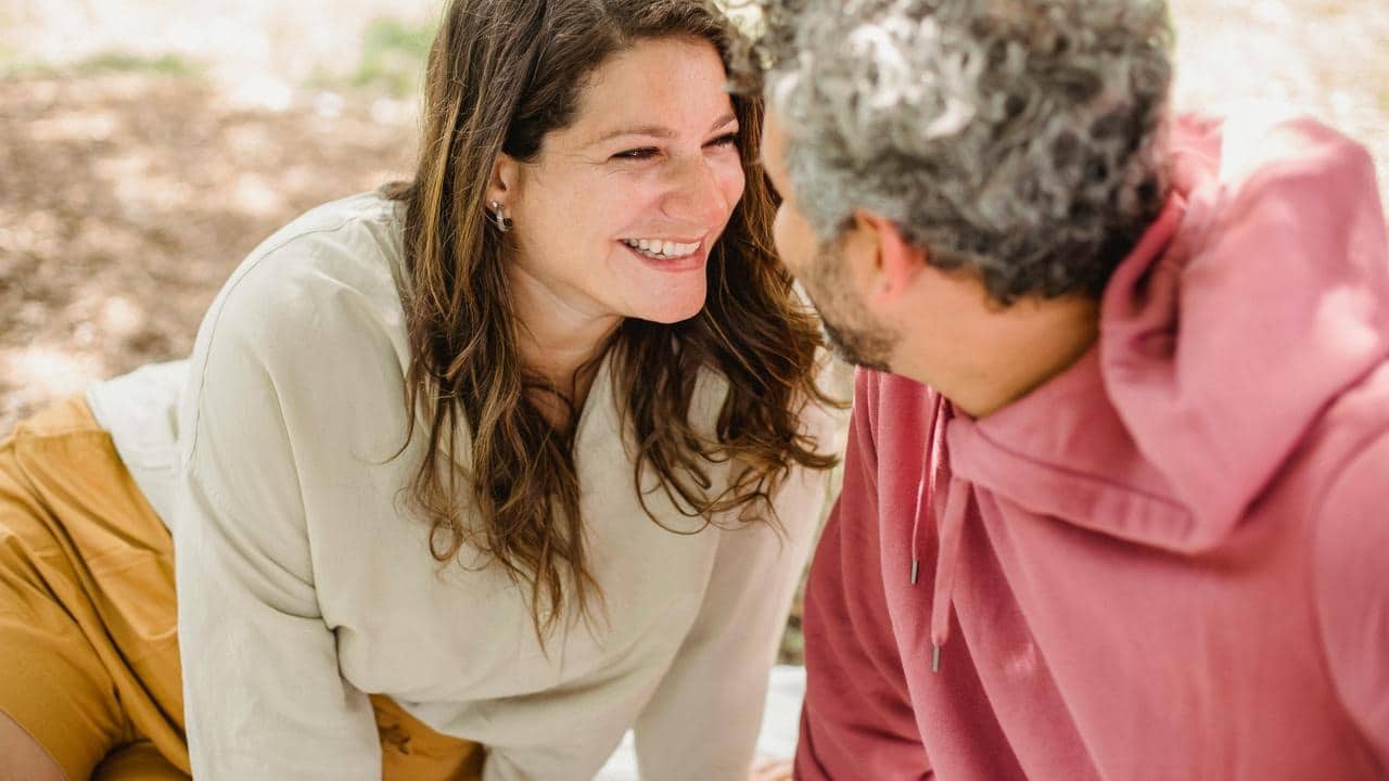 A couple sitting close together and smiling at each other outdoors.