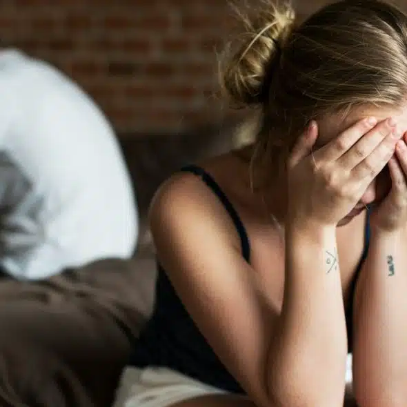 A frustrated woman is holding her head with her hands and a man is in the background.