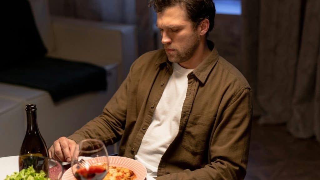 A man in a brown shirt sits at a table with a plate of food.
