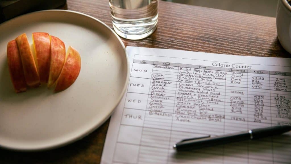 A sliced apple on a plate sits next to a handwritten weekly calorie counter chart.