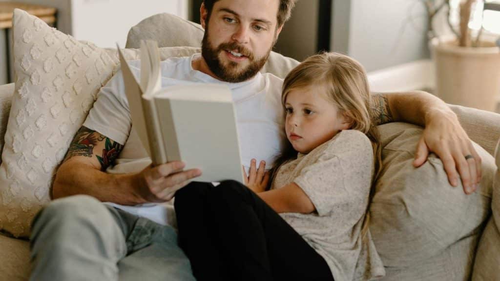 A parent reading a book with a young child on a couch at home.