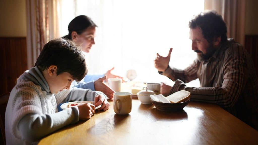 A man and woman talking at a table while a young boy looks down.