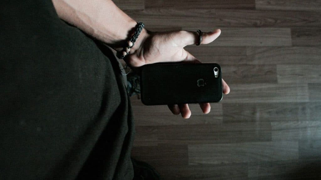 A person holding a black smartphone in their palm over a brown wood grain floor.