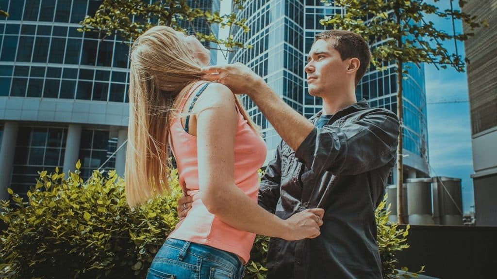 A man standing outside holding the back of a woman's neck while she leans back.