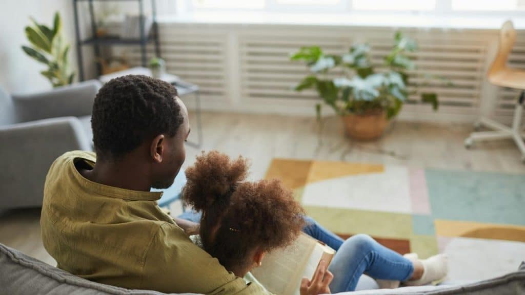 A parent and child sitting together on a couch, reading a book at home.