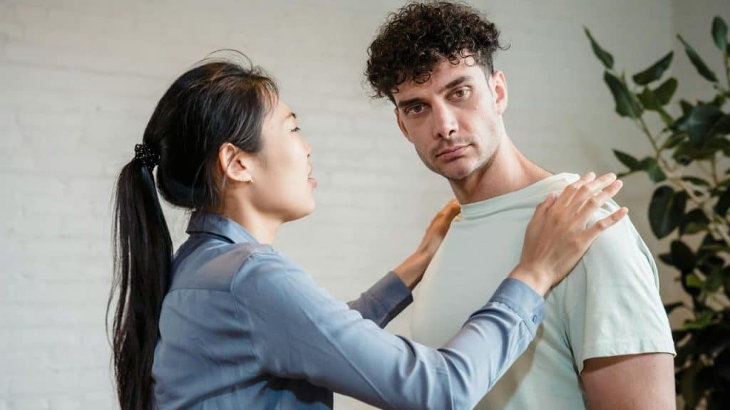 A woman with a dark ponytail places both hands on the shoulders of a curly-haired man.