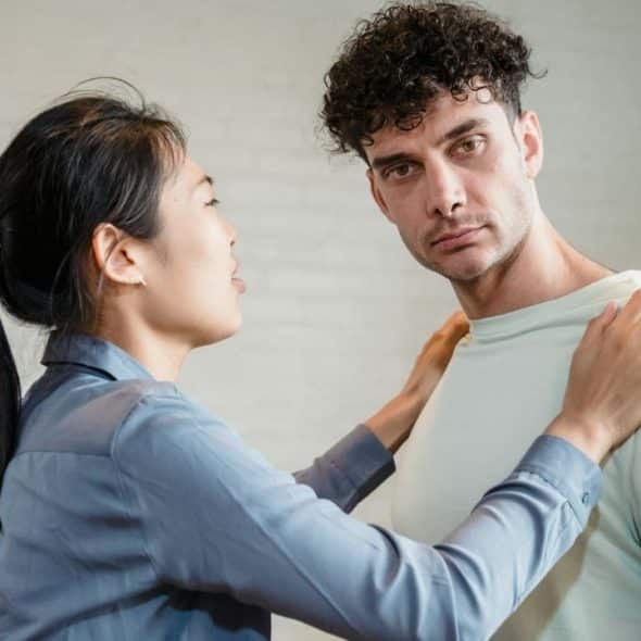 A woman with a dark ponytail places both hands on the shoulders of a curly-haired man.