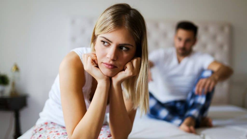 A blonde woman rests her chin on her hands while a man sits behind her.
