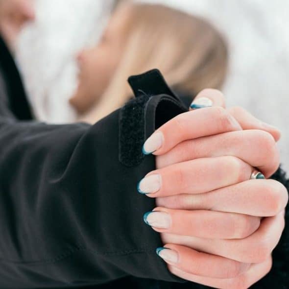A close-up of two people holding hands outdoors in winter.