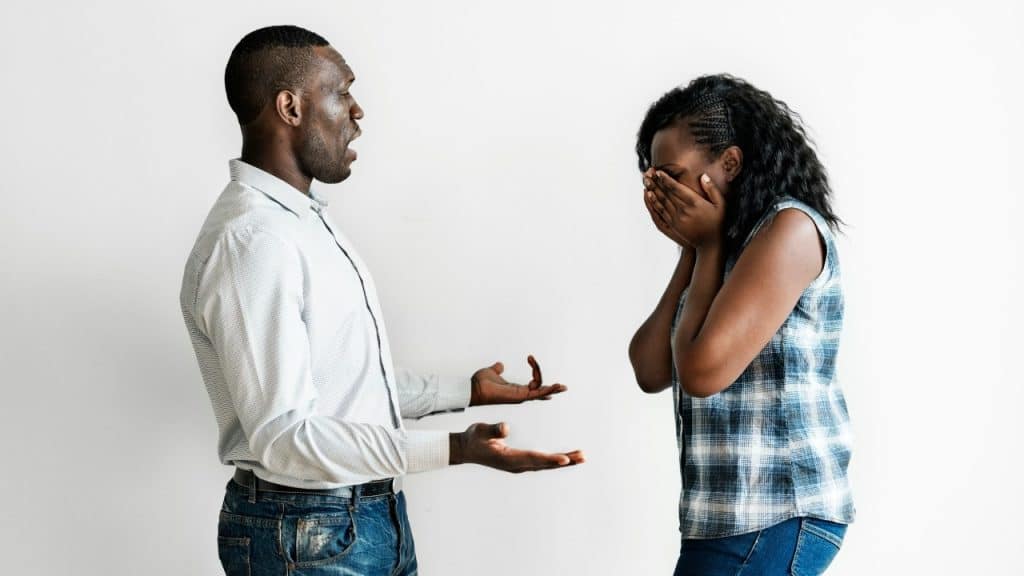 A man stands with palms up talking to a woman who is covering her face with her hands.