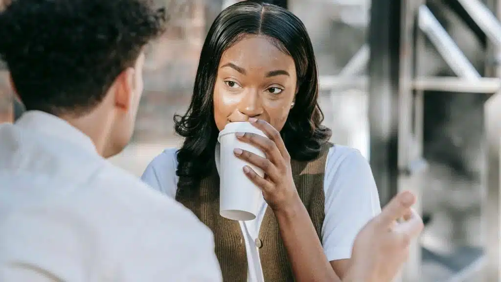 A woman is drinking coffee while talking to a man