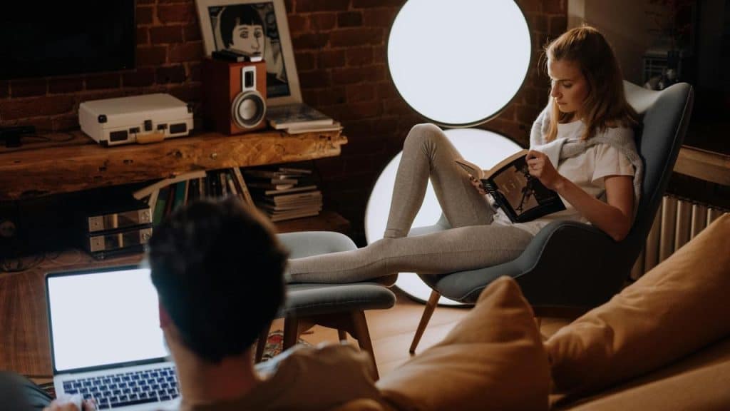 A woman reads in a chair while a man uses a laptop