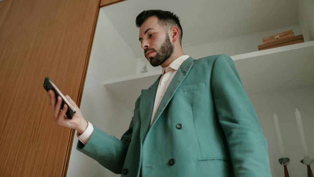 A man in a teal suit looks at his phone