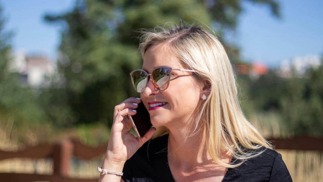 An older woman wearing sunglasses and speaking on the phone.