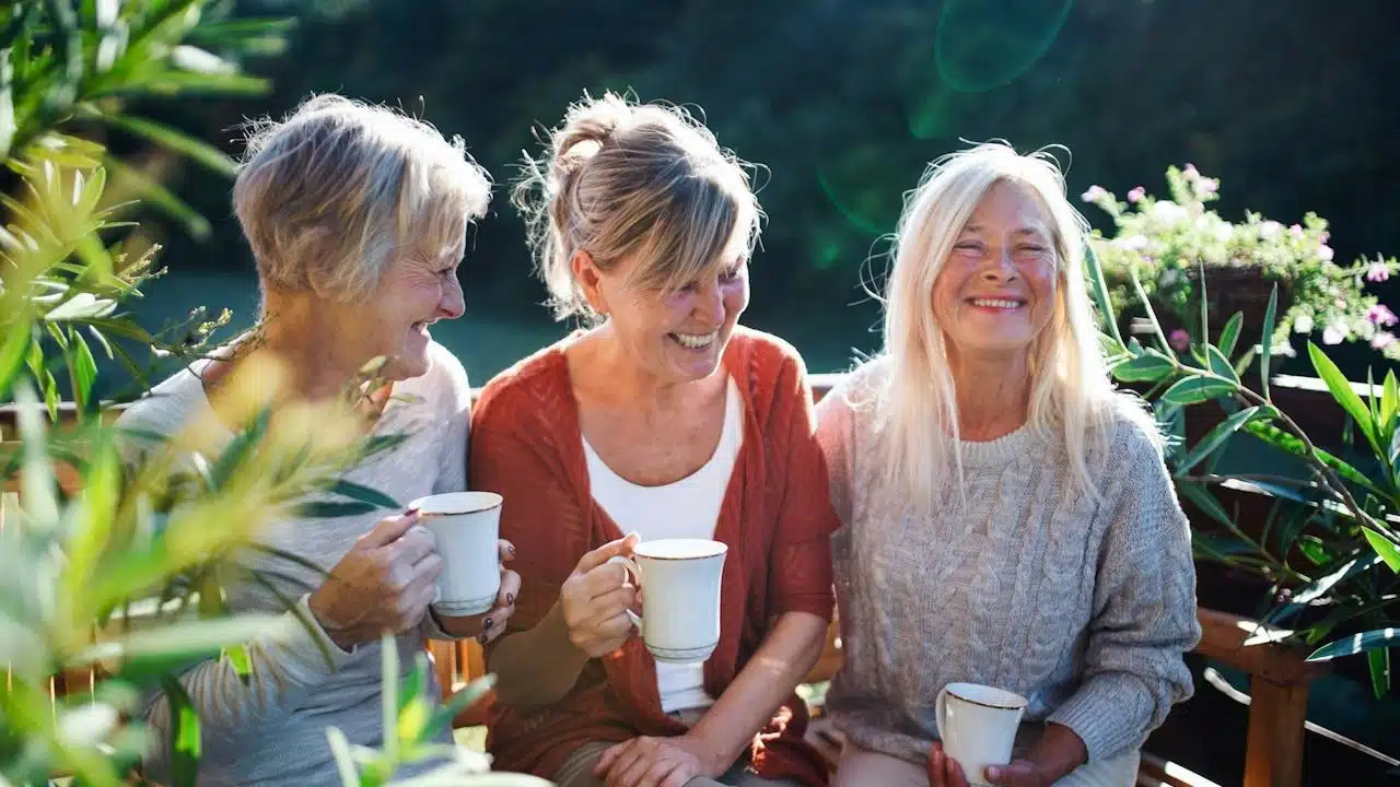 A group of mature, older friends having coffee together outdoors.