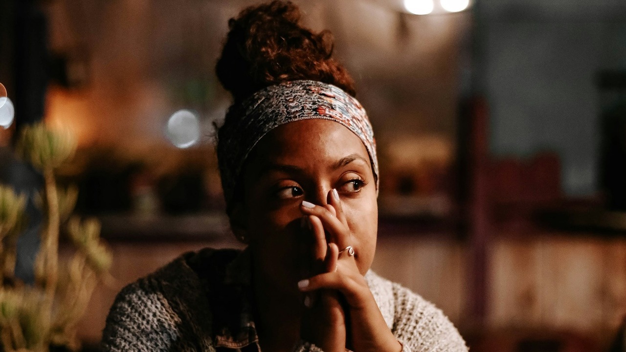 A sad woman holding her clasped hands in front of her mouth.