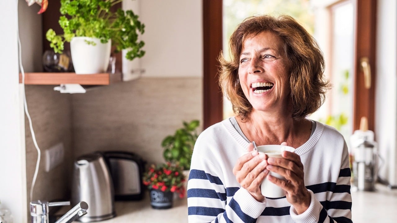 A woman laughing while holding a cup and looking to the side.