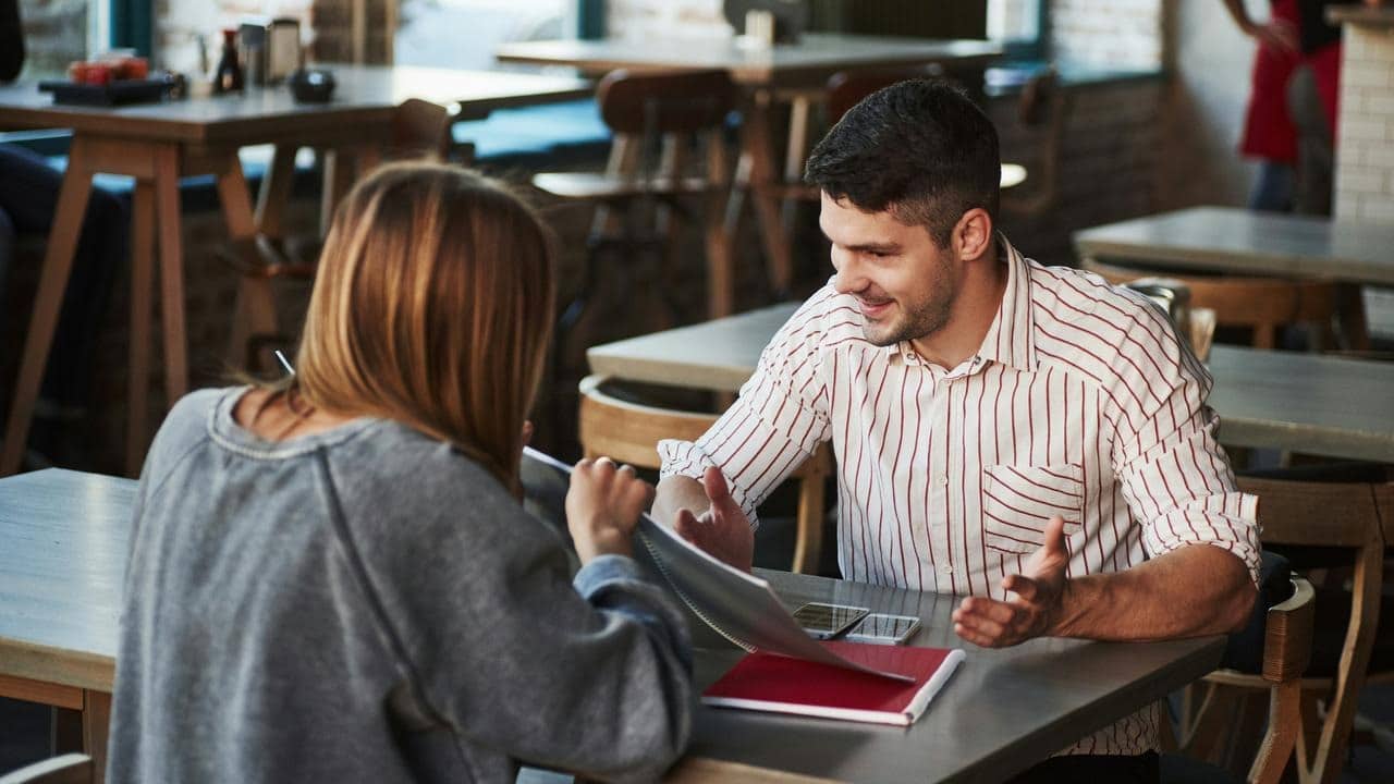 A man and woman having a discussion at a café table with notebooks.