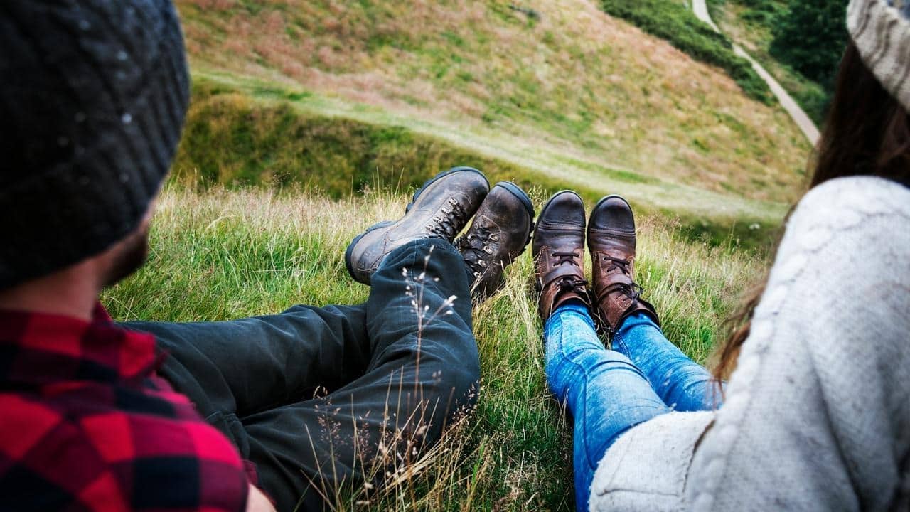 A couple relaxing on grass with hiking boots.