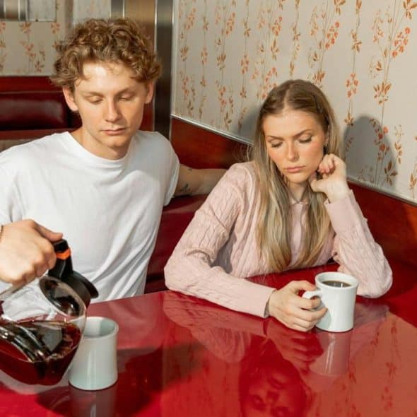 A waiter pours coffee in a mug while a couple is watching silently.