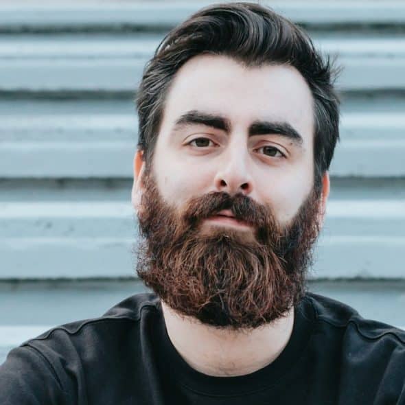 A bearded man looking at the camera with a inscrutable expression.