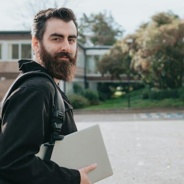 A man holding a bag and a laptop is standing outdoors.