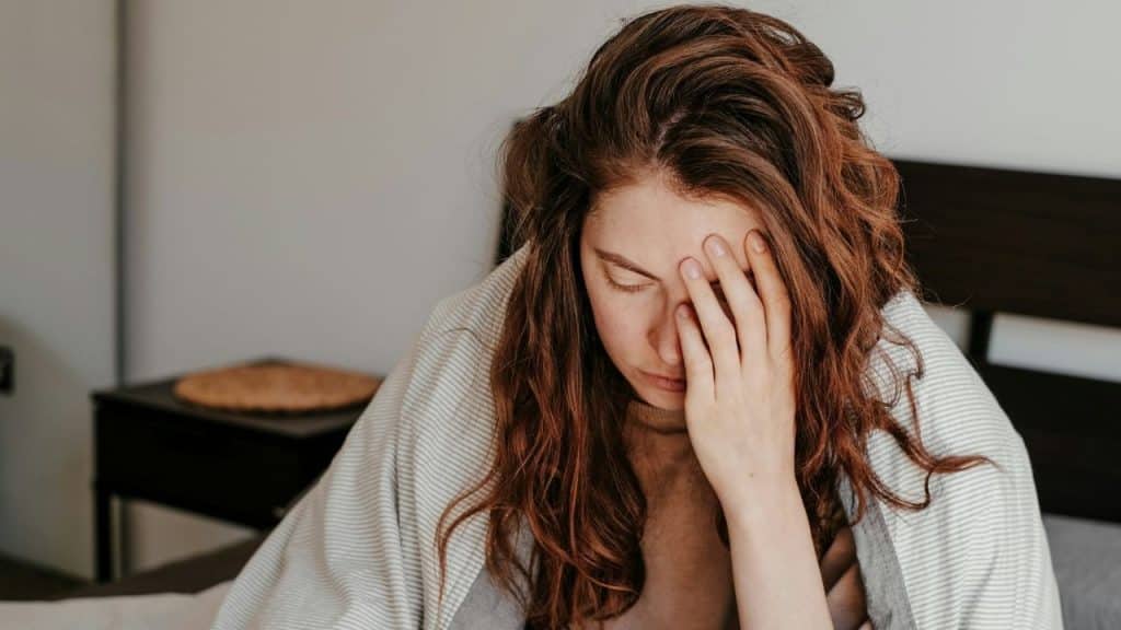 A woman with wavy hair covers her face with her hand while wrapped in a blanket.