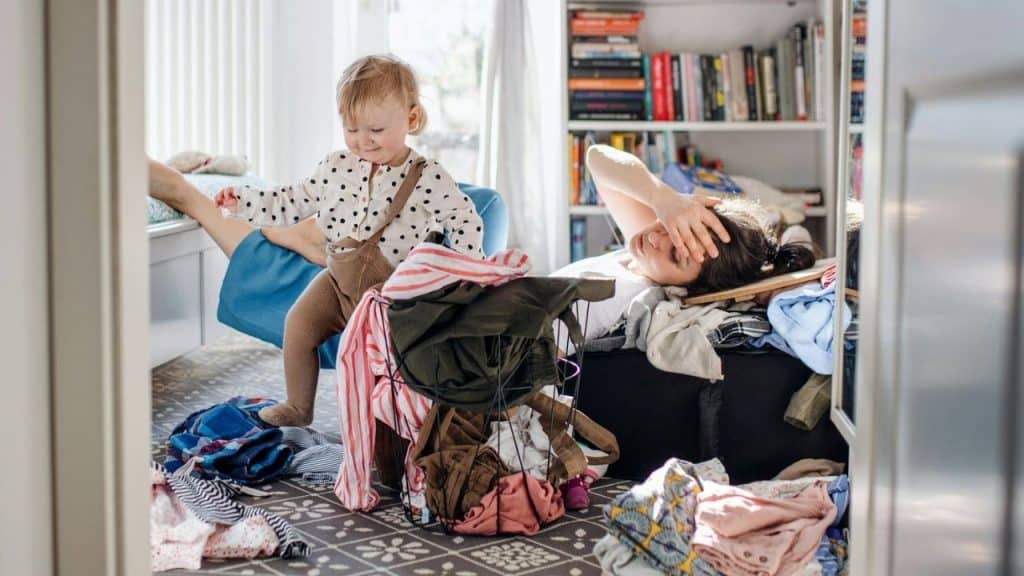 A child stands near a laundry basket while a woman lies down with her hand on her head.