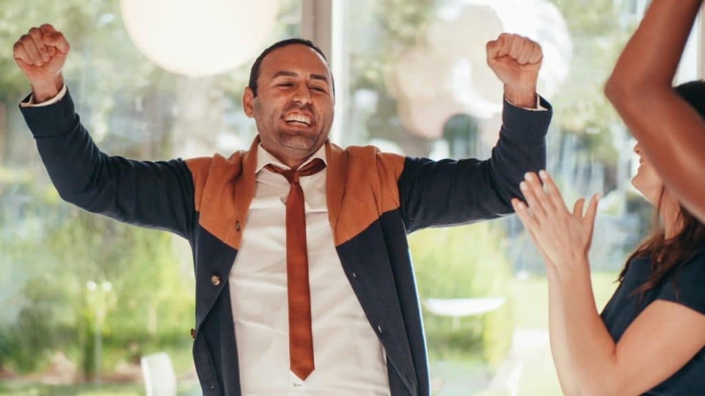A man in a tie raises his fists in the air while a woman claps.