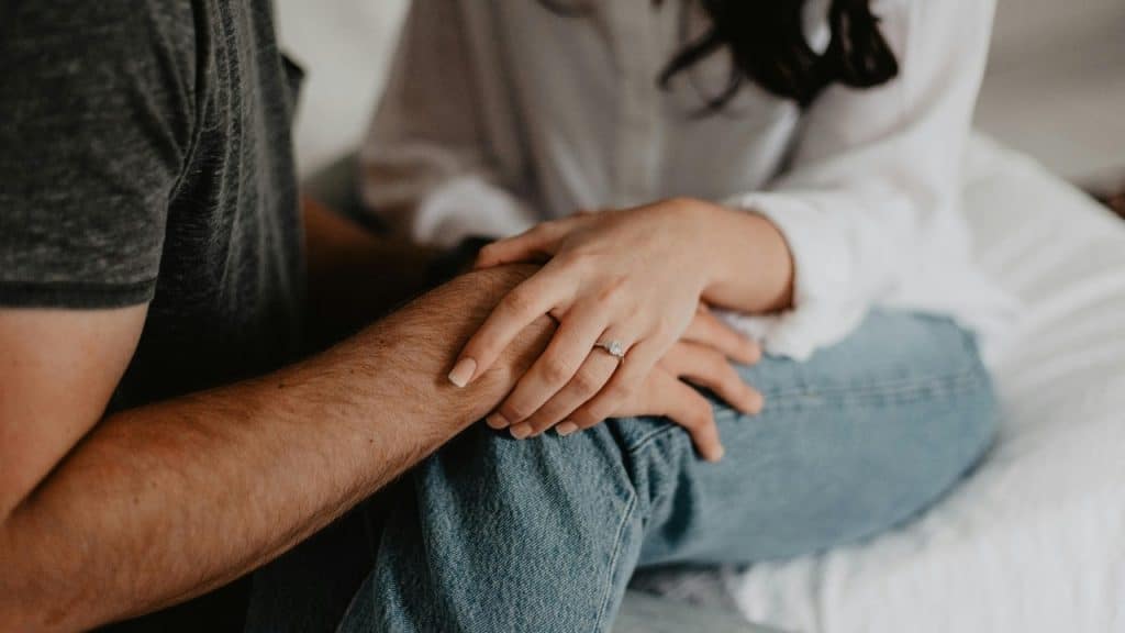 Close-up of two people sitting together, with one hand resting over the other person’s hand.