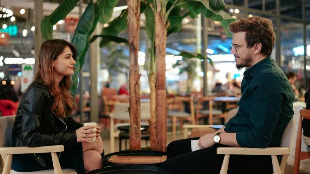 A man and woman sit across from each other at a table in a cafe.